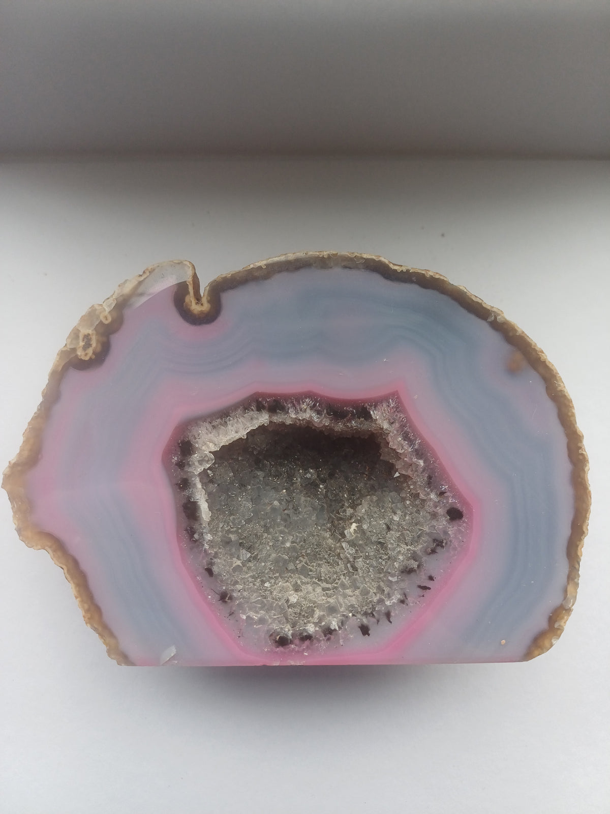 Colour-enhanced pink and blue agate geode section with central druzy quartz cavity, approximately 130 by 90mm face