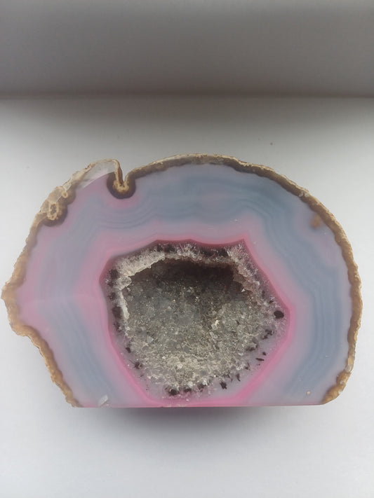 Colour-enhanced pink and blue agate geode section with central druzy quartz cavity, approximately 130 by 90mm face