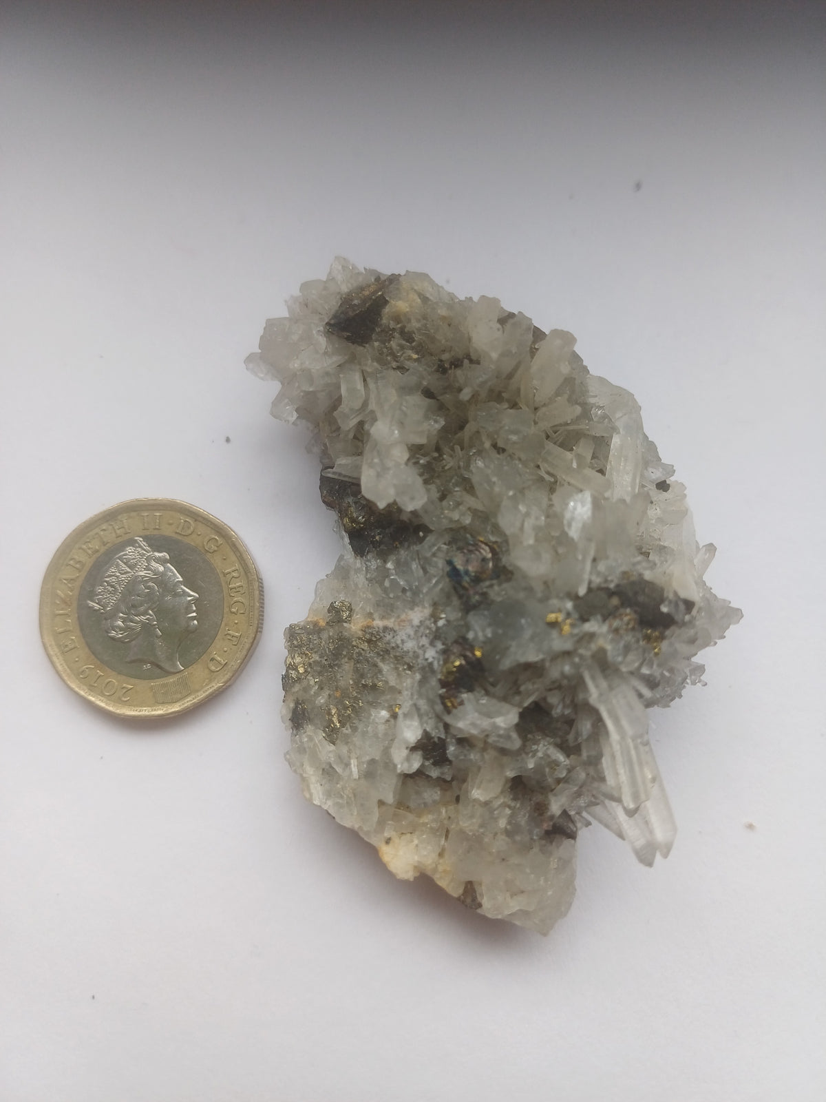 Quartz and mixed sulphide mineral specimen beside a UK one pound coin for scale